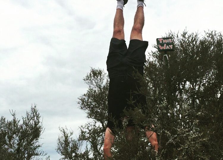 man doing handstand near bushes