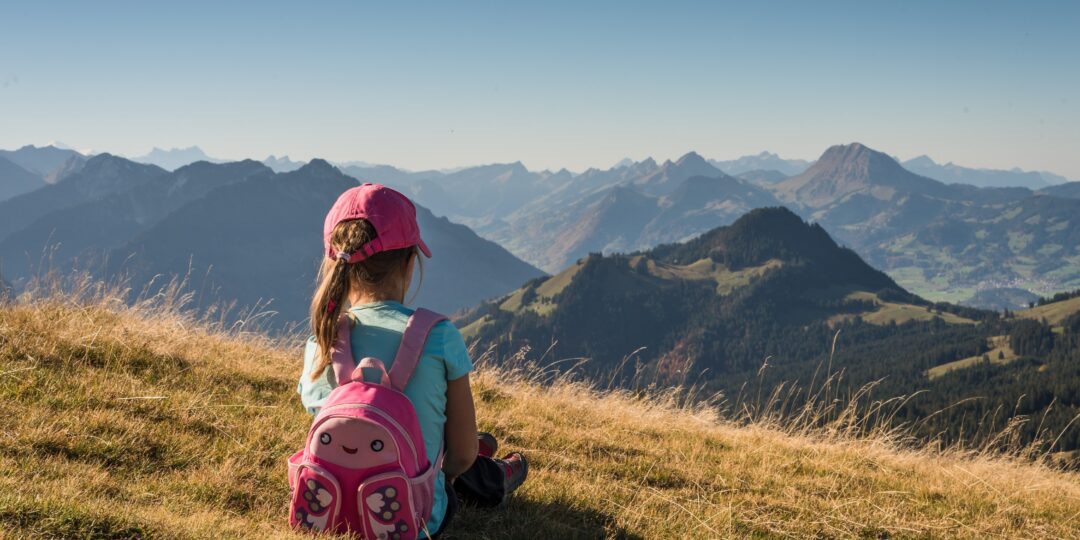 Girl sitting on hillside looking at mountains while wearing a backpack