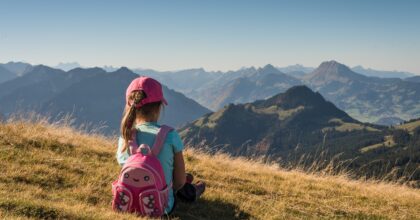 Girl sitting on hillside looking at mountains while wearing a backpack