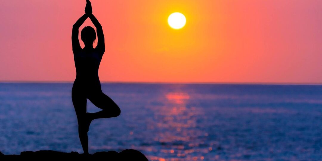 Woman practicing yoga in tree pose during sunrise